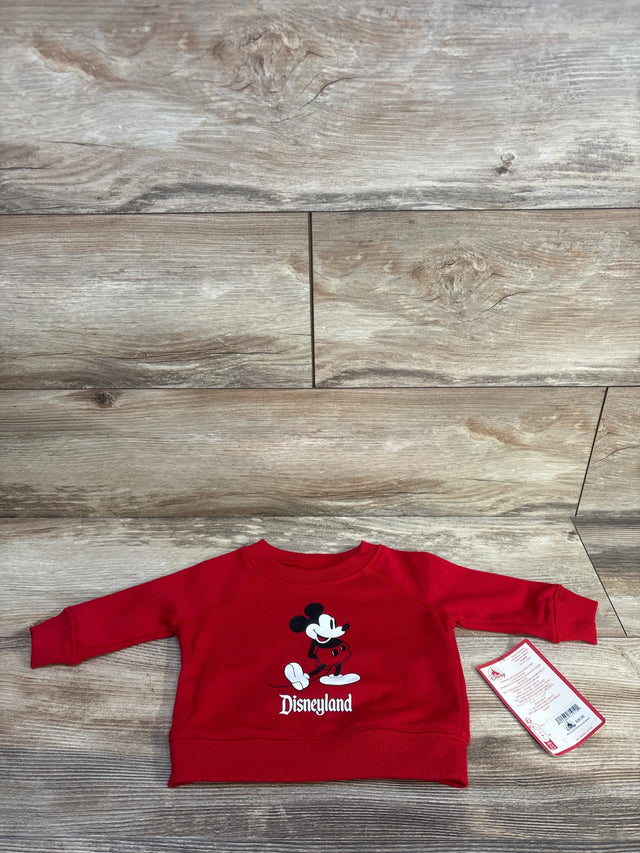 Front view of red baby sweatshirt with Mickey Mouse graphic and "Disneyland" text, ribbed cuffs and hem, size 3-6M tag on wood floor