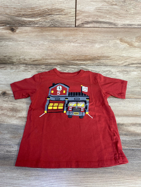 Front view of red Children's Place fire station t-shirt showing a firehouse and fire truck graphic with HERO plate on wood floor