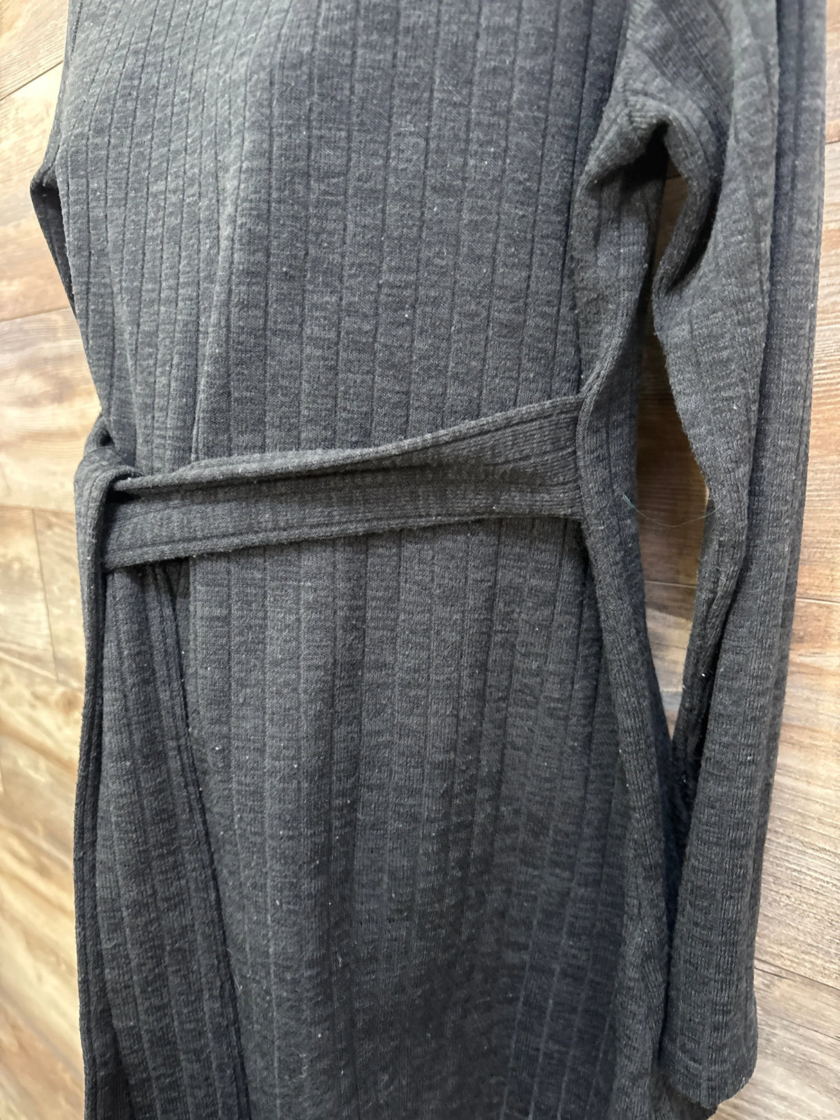 Close-up front of Ekouaer black ribbed maternity long-sleeve dress with waist tie on wooden background