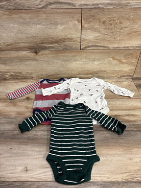 Three long-sleeve baby bodysuits on wooden floor: green striped, red and gray striped, and white with small prints