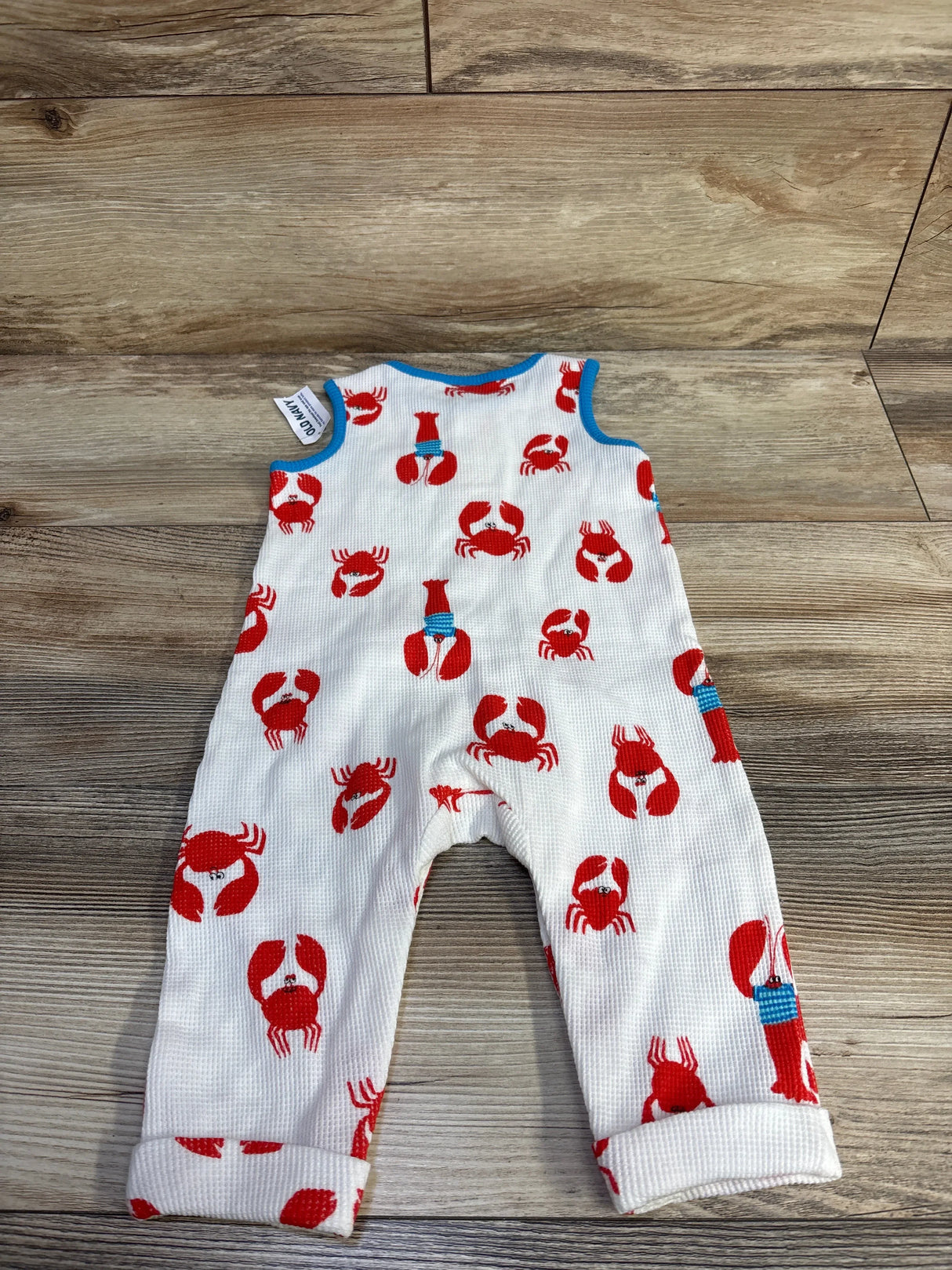 Flat-lay of Old Navy sleeveless waffle-knit henley jumpsuit showing red crab print, blue trim, and rolled cuffs on wood floor