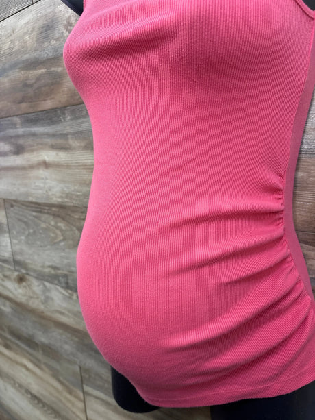 Side view of Old Navy maternity ribbed tank top in hot pink showing side ruching over belly on mannequin against wood wall