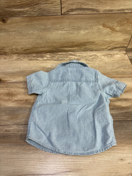 Back view of OshKosh blue chambray button-up shirt in size 12 months showcasing short sleeves and curved hem on a wood floor