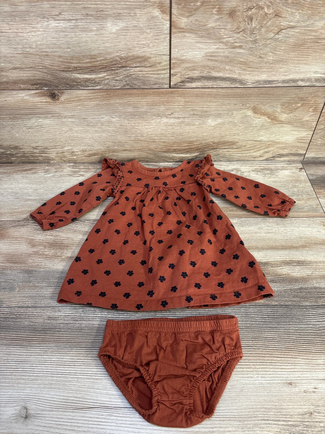 Flat lay of rust brown long sleeve baby dress with black floral print and ruffled shoulders, plus matching bloomers on wood