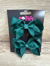 Front view of two medium green grosgrain hair bows on a branded black card with wood plank background