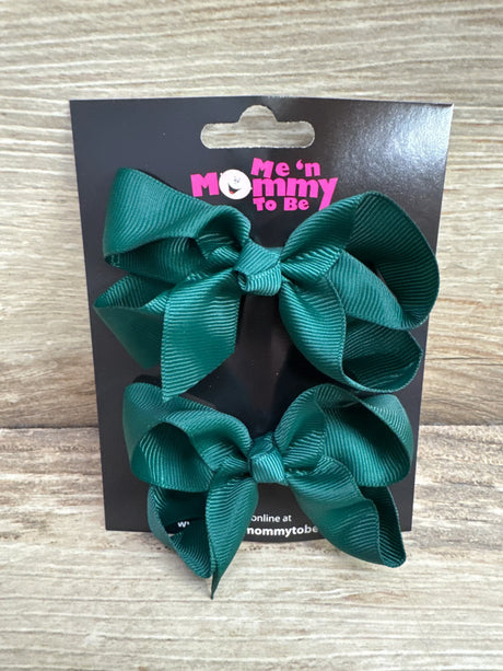 Front view of two medium green grosgrain hair bows on a branded black card with wood plank background
