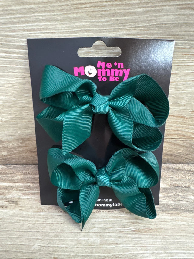 Front view of two medium green grosgrain hair bows on a branded black card with wood plank background