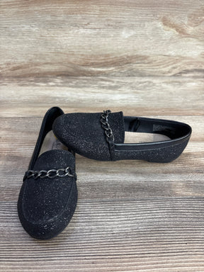 Pair of black glitter loafers with metal chain detail on wood surface