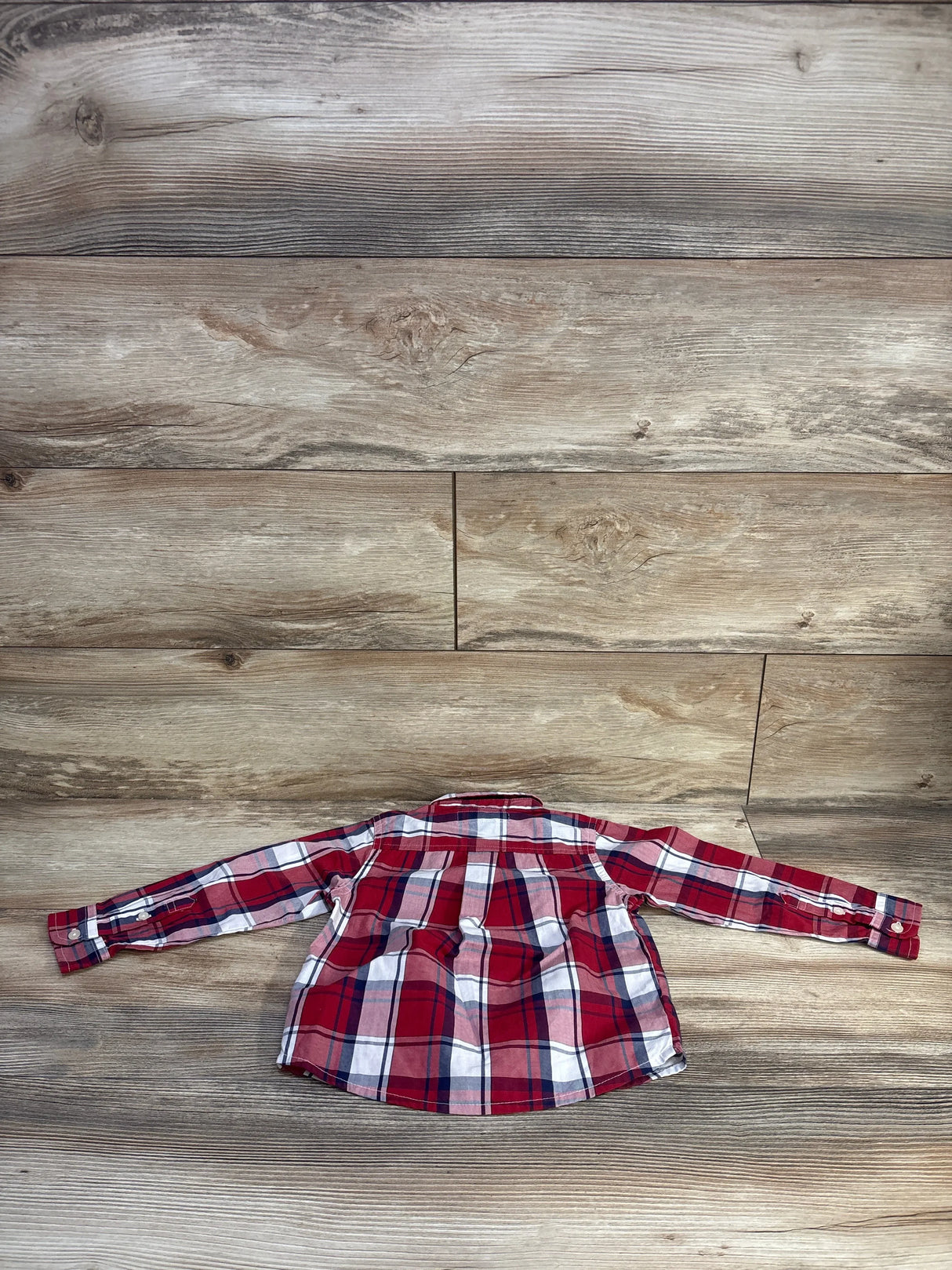 Back view of toddler red plaid long-sleeve button-up shirt showing pleated back yoke and button cuffs on wood background