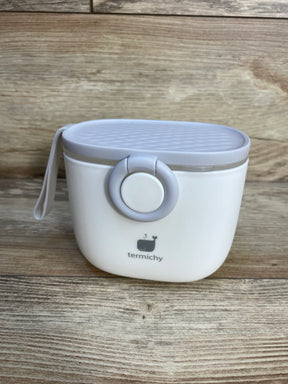 Front view of Termichy baby formula dispenser with gray textured lid, front button latch and side strap on wooden tabletop