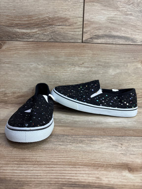 Pair of black kids slip-on shoes with multicolor sparkly sequins and white rubber soles on wooden floor