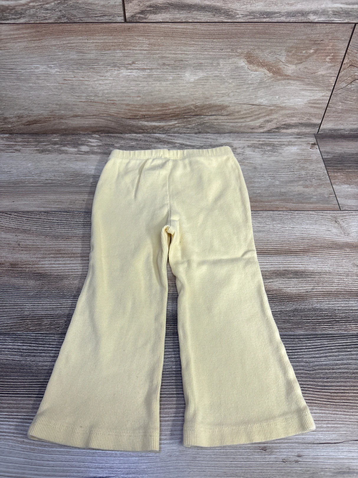 Flat lay of yellow Baby Gap ribbed flare leggings, size 18-24 months, showing elastic waist and flared legs on wood floor