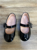 Black patent leather girls' dress shoes with bows, Mary Jane style, on wood floor