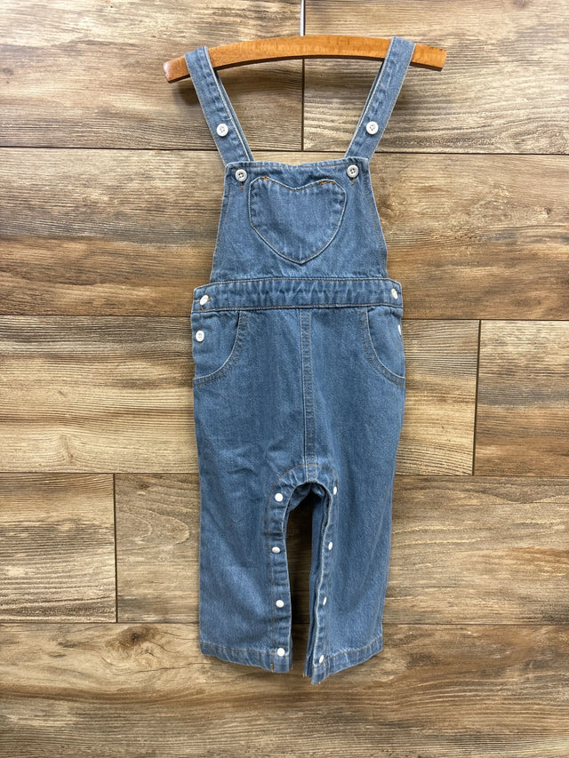 Blue denim toddler overalls with heart-shaped chest pocket and snap closures, hanging on wooden hanger