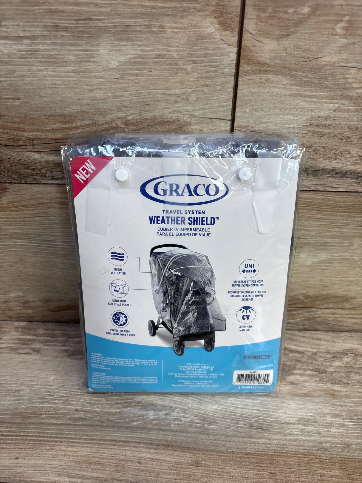 Front of Graco Weather Shield packaging showing clear rain cover on stroller, wood background