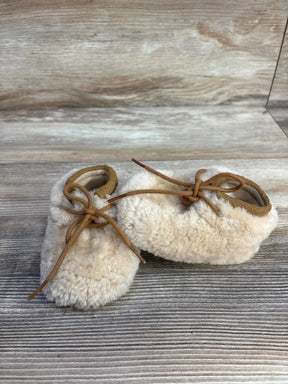 Cream shearling baby booties with tan laces on rustic wooden background
