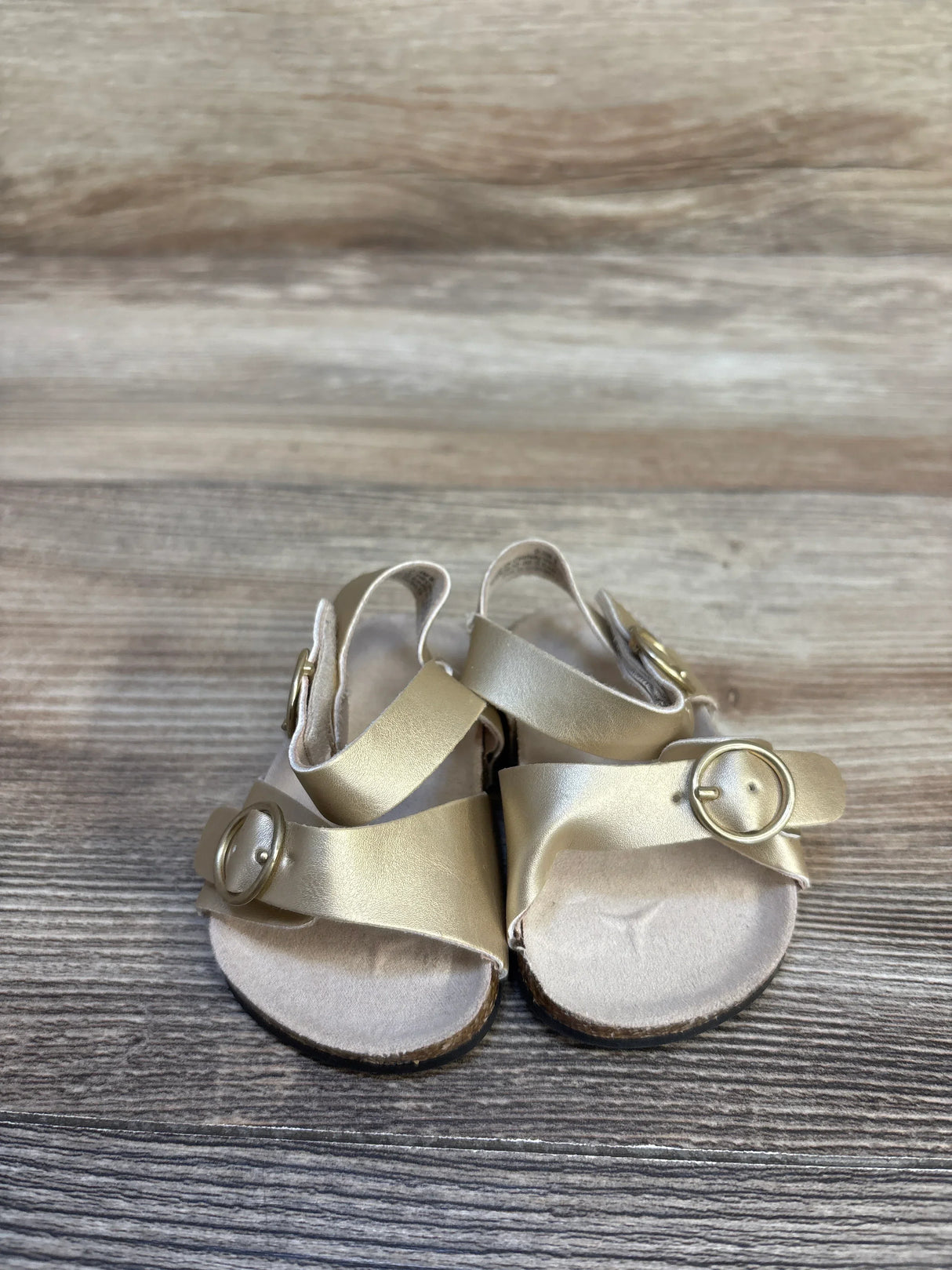 Gold toddler sandals with buckle straps on wooden background, gently used kids footwear