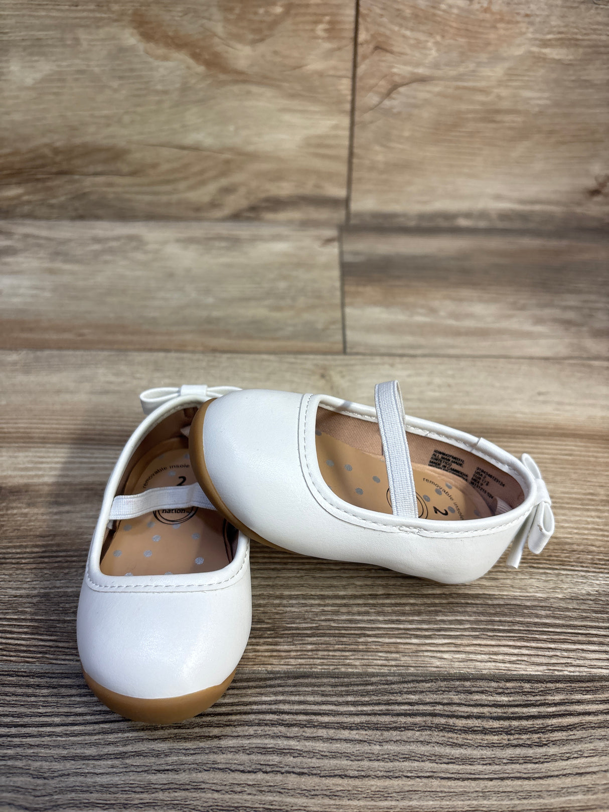 Front and side view of Wonder Nation girls white bow ballet shoes showcasing elastic strap, back bow, and tan sole on wood floor