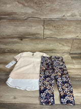 Flat lay of 2-piece toddler outfit showing cream top with white layered hem and keyhole back; navy floral leggings on wood floor