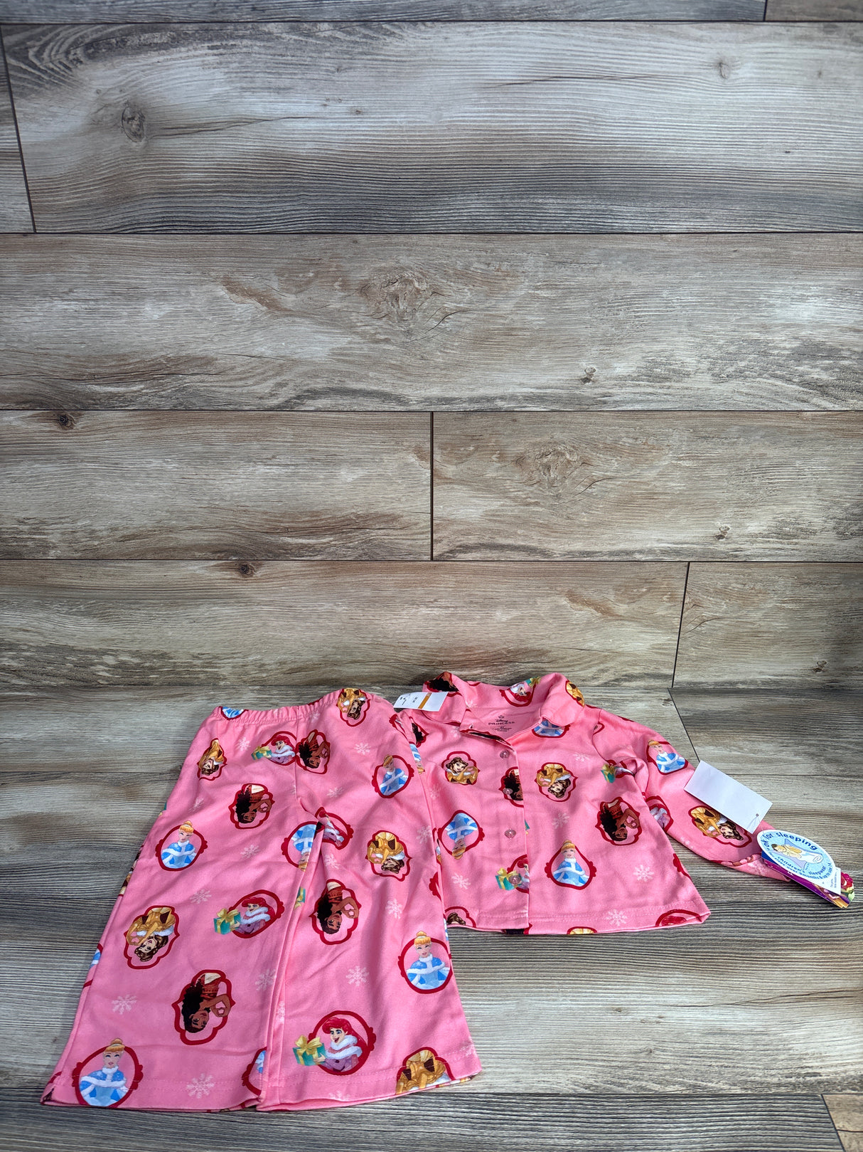 Front view of girls' pink Disney Princess 2pc button-up pajamas with button-front top and elastic pants on wood floor