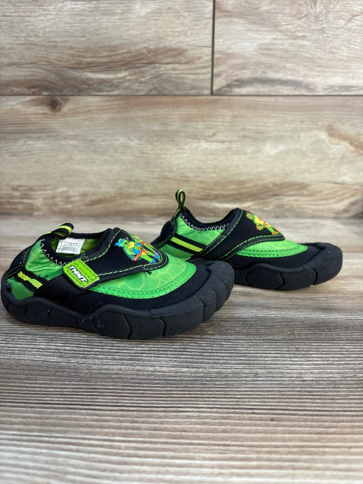 Green and black toddler slip-on shoes with cartoon turtle design on wood background