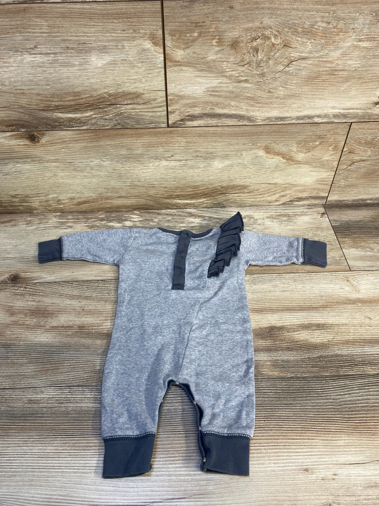 Gray baby romper with dark ruffle detail on chest, laid flat on wood background