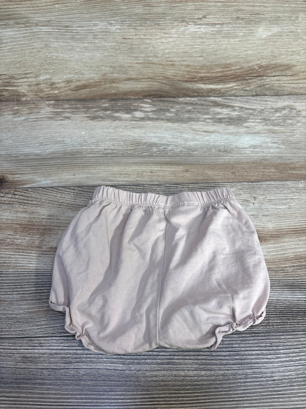 Top view of beige H&M cotton jersey baby bloomers showing elastic waistband and gathered leg openings on wood background