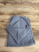 Top-down view of Comfy Cubs muslin car seat cover folded to show soft crinkled texture and elastic strap on wood background