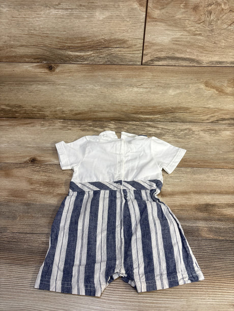 Flat lay of white baby romper with navy vertical striped suspender shorts and back buttons on wooden floor