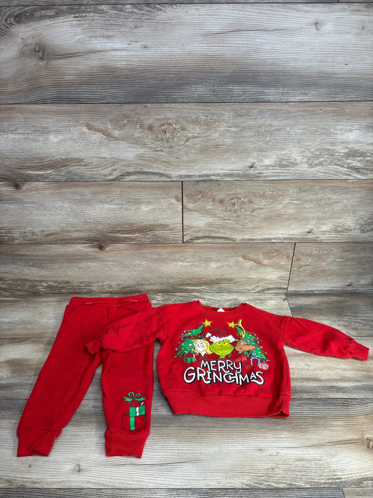 Red Grinch-themed toddler Christmas outfit with 'Merry Gringmas' sweater and gift-print pants on wood floor