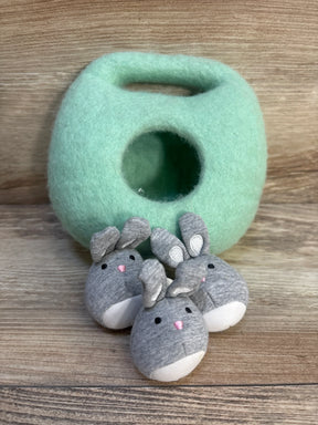 Plush green felt bunny house with three small gray fabric bunny toys on wood background