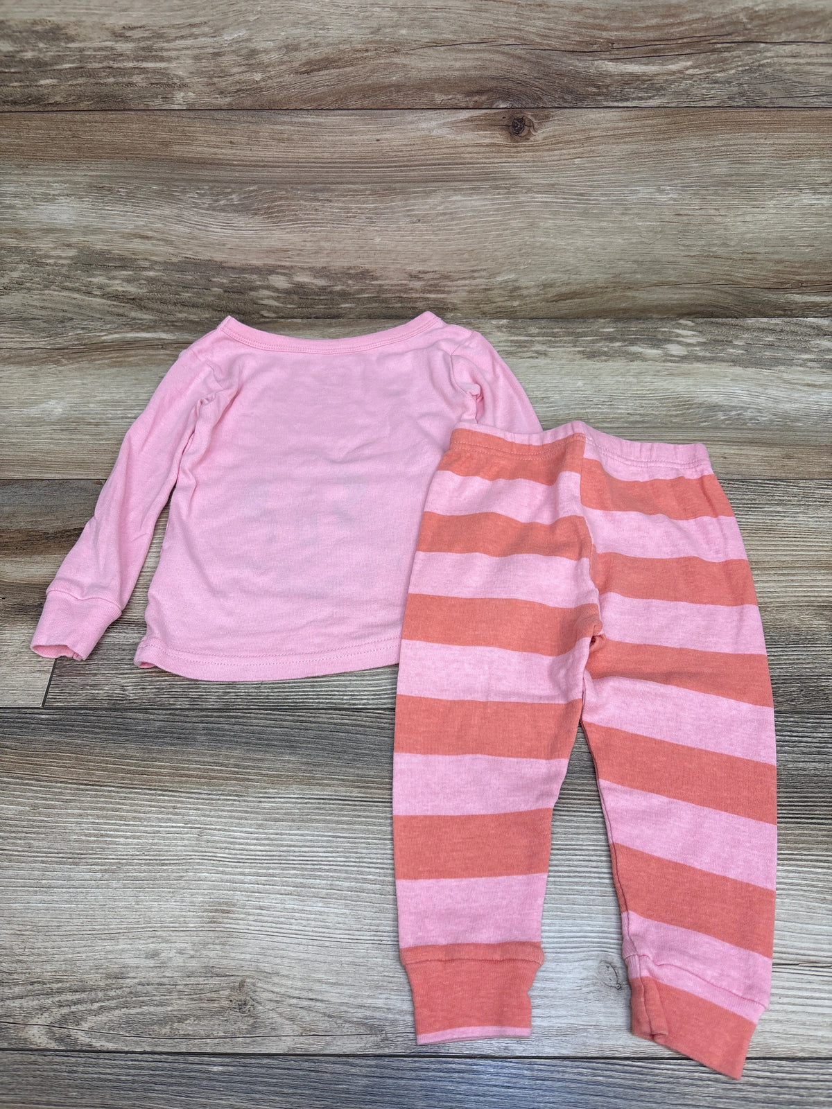 Top-down view of Disney Junior Minnie Mouse pink two-piece pajama set with solid top and striped pants on wood-grain background