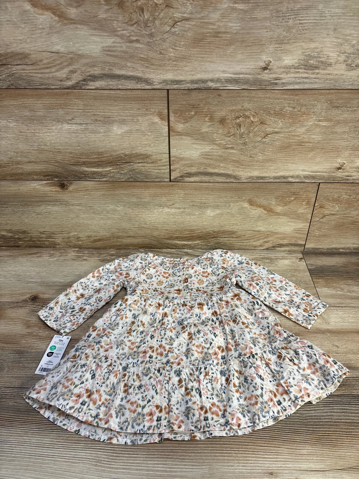 Flat lay of OshKosh white floral smocked long-sleeve dress and bloomers set showcasing smocked bodice and tiered skirt on wood background