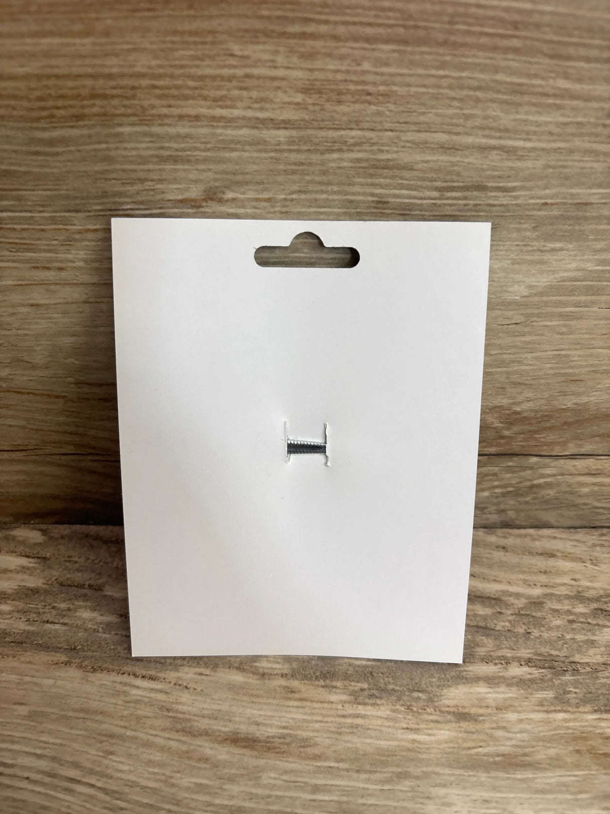 Front view of Barbie hair bow pink packaging showing blank white hang card with small silver fastener on wood background