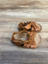 Brown toddler sandals with floral cutout straps on wood background