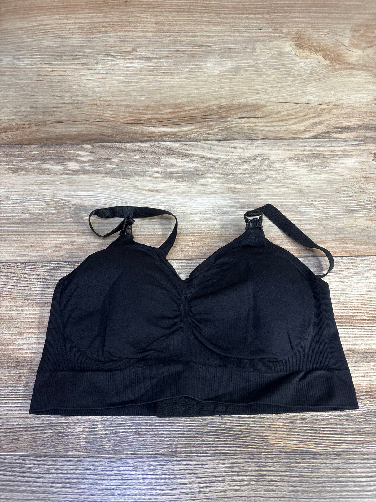 Flat lay of black nursing bra showing front drop-down nursing clips, molded cups, and wide underband on wood background
