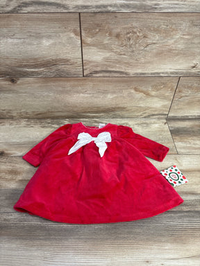Red long-sleeve baby dress with white bow detail, laid on wood background