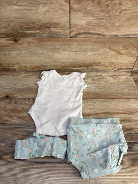 Flat lay of Catherine Malandrino 3 piece baby set: white ribbed bodysuit, blue floral bottoms and headband on wood