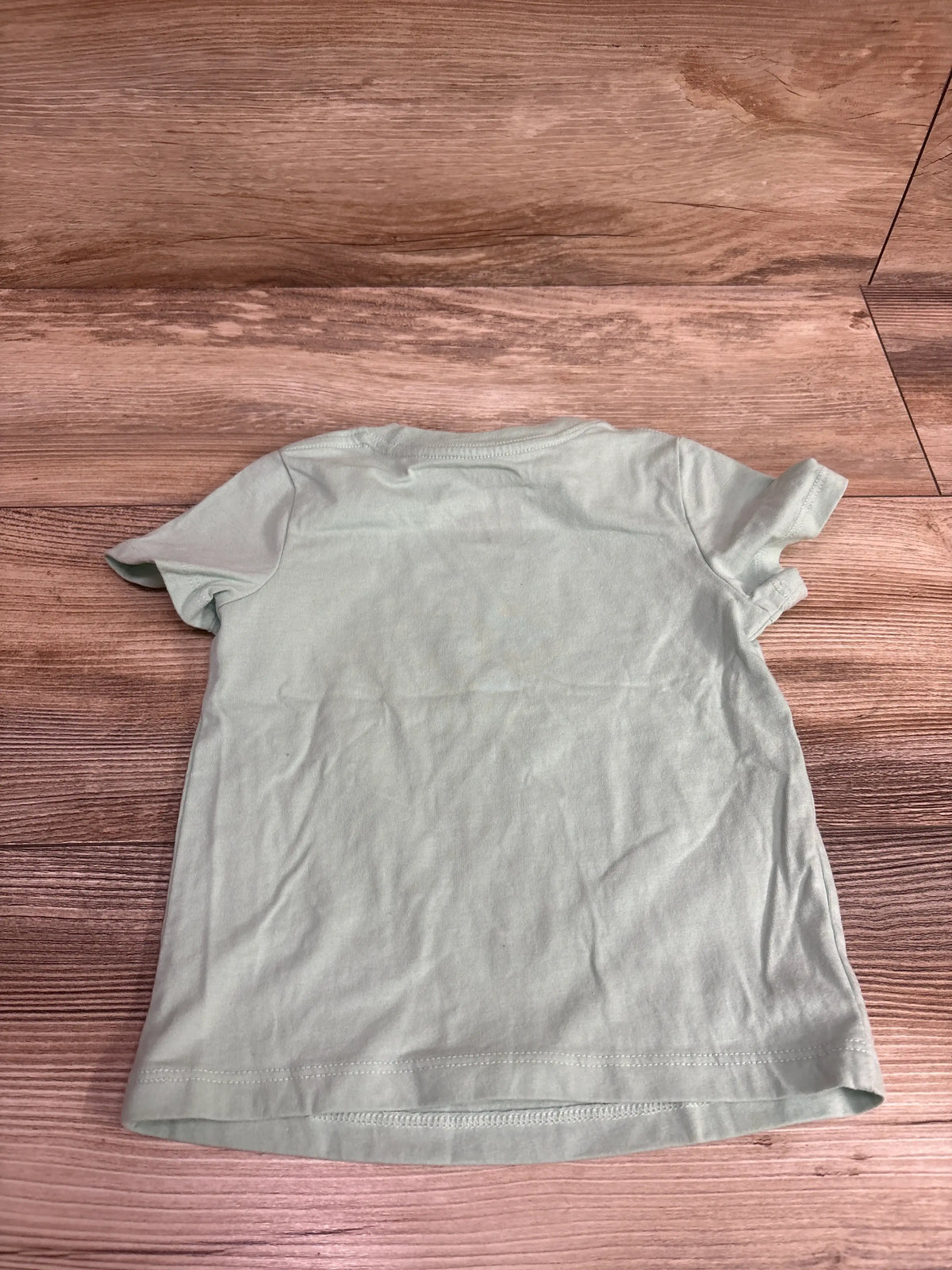 Back view of a light green Cat & Jack baby shirt size 18m on a wooden surface