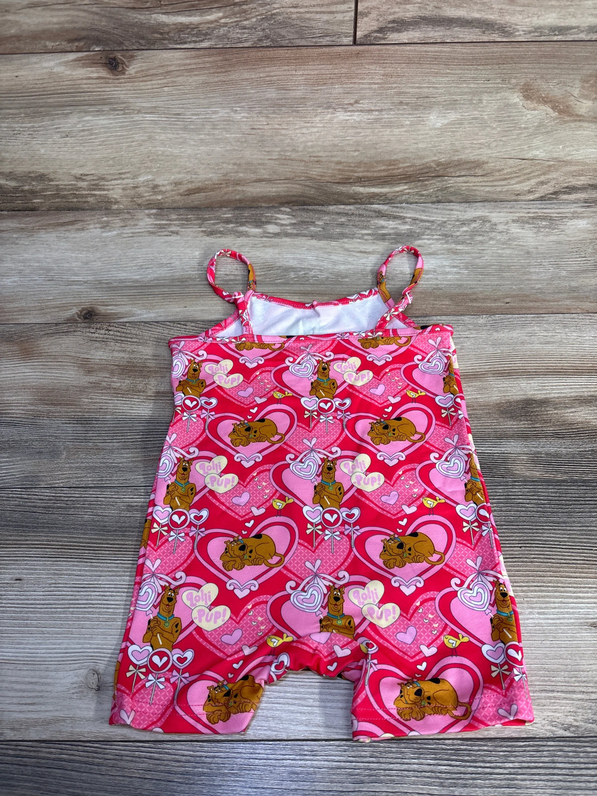 Flat lay of pink Shein x Scooby‑Doo shortie romper (2T) showing heart and Scooby‑Doo print on wood background