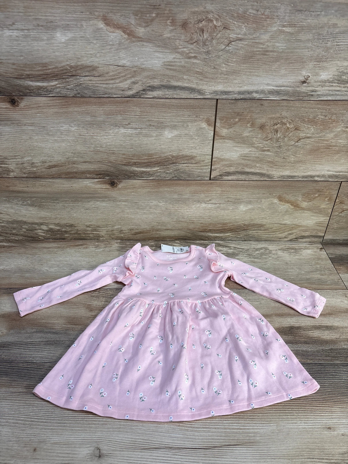 Flat lay of pink long-sleeve floral toddler dress with ruffle shoulders and gathered skirt on wood background