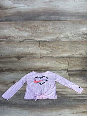 Flat lay of pink Nike toddler long-sleeve tie-front shirt (4T) showcasing heart-shaped Nike swoosh logo and knotted front on wood background