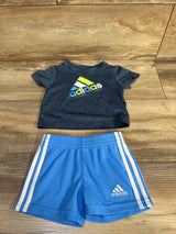 Flat lay of boys' Adidas two-piece set showing navy logo tee and light blue shorts with white side stripes on wood background