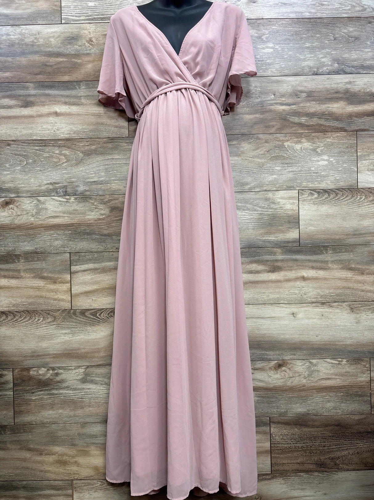 Front view of blush maternity maxi dress (XL) with V-neck wrap, braided waist, and flowing skirt against wood background