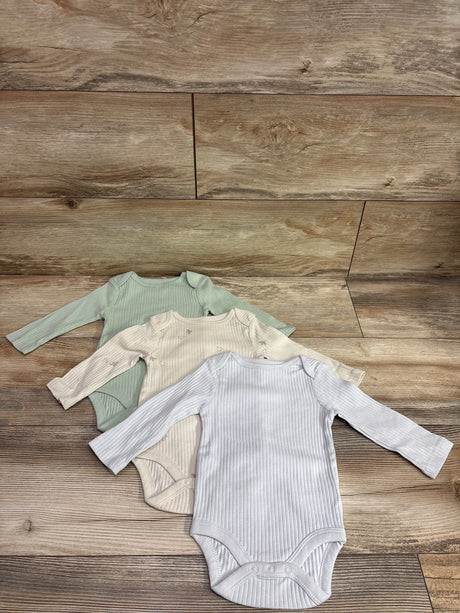 Top-down view of Cloud Island three-pack ribbed long-sleeve bodysuits in green, cream, and light blue on a wood background