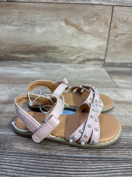 Three quarter view of Cat and Jack blush toddler sandals with pearl accented crossover straps and ankle Velcro on wood floor