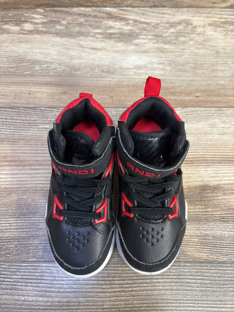 Top-down view of toddler AND1 black basketball sneakers with red accents, lace-up front and Velcro ankle strap on wood floor
