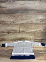 Back view of gray, white, and navy blue long-sleeve toddler shirt on wooden floor background