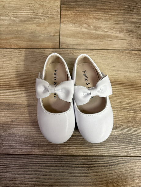 Top view of Felix and Flora white Mary Jane shoes showcasing large bows on a wood floor