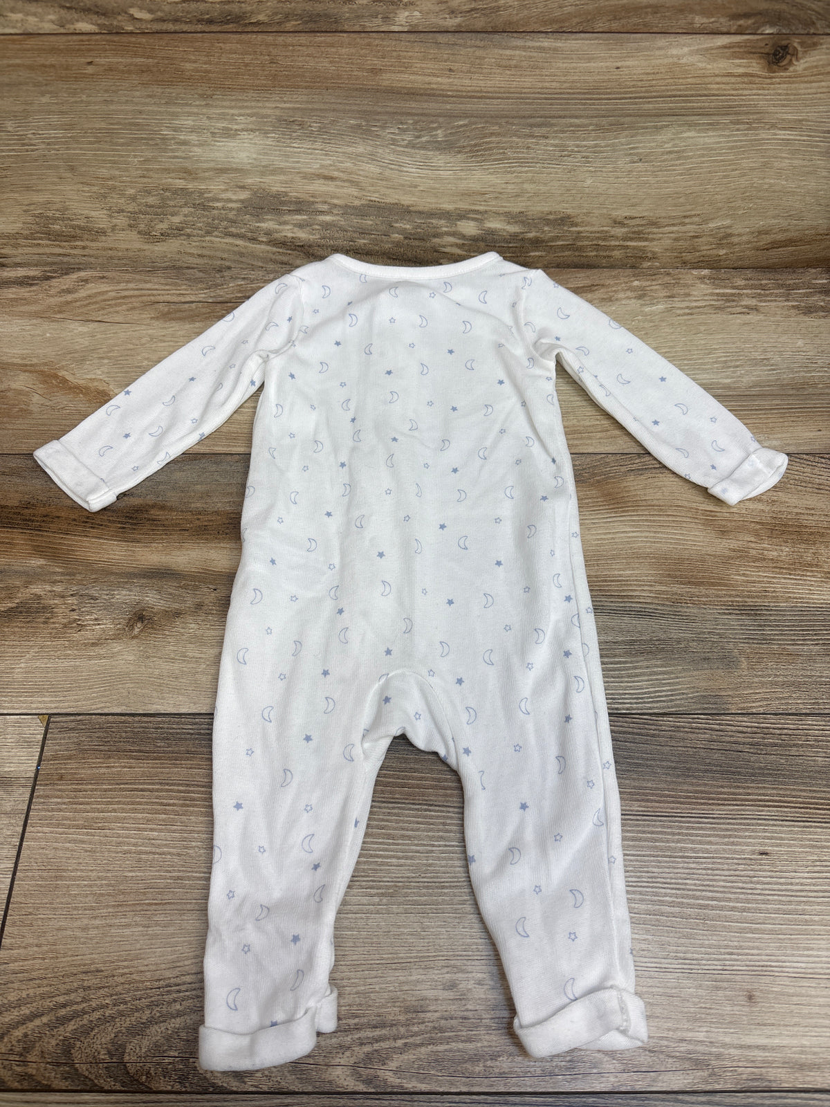 Front view of Child of Mine white sleeper in size 3 to 6 months, showcasing moon and star print and long sleeves on a wood background